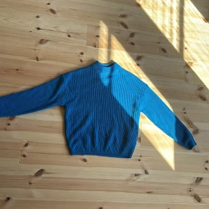 Blå stickad tröja - Säljer en snygg blå stickad tröja som är perfekt för kyligare dagar. Tröjan har en normal passform och långa ärmar. Den är ribbad vilket ger en fin textur och extra stilpoäng. Perfekt för både höst och vinter!