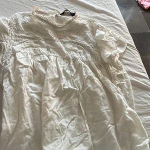 Vit klänning från Vero Moda - Säljer en superfin vit tröja från Vero Moda. Den har vackra spetsdetaljer och en lös passform som gör den perfekt för sommardagar. tröjan är kortärmad och har en romantisk stil. Perfekt för både vardag och fest!