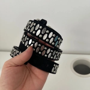 Svart bälte med silverdetaljer från Pieces - Säljer ett snyggt svart bälte från Pieces med coola silverdetaljer. Bältet har en stilren design med små silvernitar som ger en rockig känsla. Perfekt för att piffa upp vilken outfit som helst! Spännet är också i silver och ger en fin kontrast mot det svarta materialet. helt ny aldrig använt.