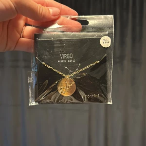 Guldpläterat halsband med Jungfrun stjärntecken från Montini - Snyggt guldpläterat halsband från Montini/Ur & Penn med en rund berlock som har Jungfrun stjärntecken ingraverat. Perfekt för dig som är född mellan 23 augusti och 22 september. Halsbandet är i en enkel stil. 
