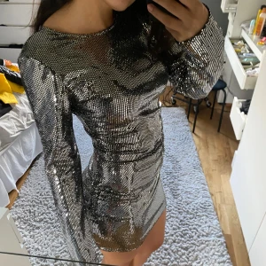 Glittrig silverklänning - Säljer en superglittrig och snygg silverklänning som verkligen fångar ljuset! Den är tight och kort, perfekt för en fest eller nyår. Klänningen har långa ärmar och är täckt med paljetter som ger en fantastisk effekt. Perfekt för dig som vill sticka ut och glänsa! ✨