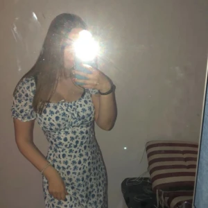 Blommig klänning med puffärmar - Säljer en superfin vit klänning med blått blommönster. Den har söta puffärmar och en smickrande passform. Perfekt för sommarens alla fester eller en mysig picknick i parken. Klänningen är i bra skick, bara använd 2 gånger.