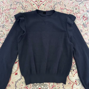 Stickad tjocktröja - Mörkblå med volanger. Storlek S. Är i nyskick.