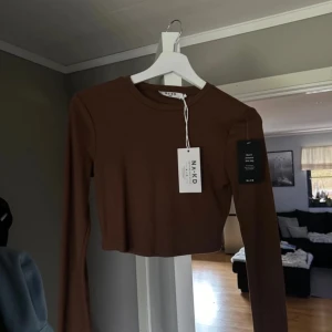Brun croppad tröja från NA-KD - Säljer en snygg brun croppad tröja från NA-KD. Perfekt för höst och vår med sin långa ärmar och mjuka bomullsmaterial. Tröjan har en stilren design som passar både till vardags och fest. Storlek S. Helt ny med prislapp kvar.