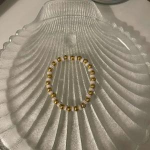Guld och vit pärlarmband - Snyggt armband med växlande guld- och vitfärgade pärlor. Perfekt för att ge en elegant touch till din outfit, oavsett om det är till vardags eller fest. Elastiskt band för enkel passform.