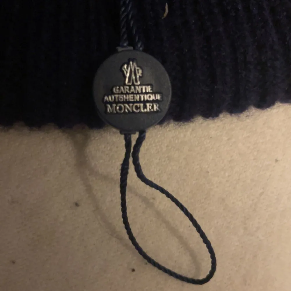 Säljer en snygg svart stickad mössa från Moncler. Den är i nyskick och har en broderad logga framtill. Perfekt för kalla höst- och vinterdagar. Mössan är navy blue och ger en skön passform. Äkta!!!!. Accessoarer.