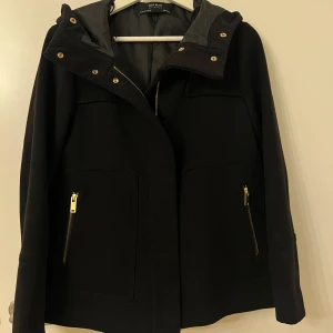 Zara Basic svart kappa storlek XS - Svart kappa med huva och guldfärgade detaljer. Kappa har fickor och dragkedja framtill.  storlek XS  samfraktar gärna