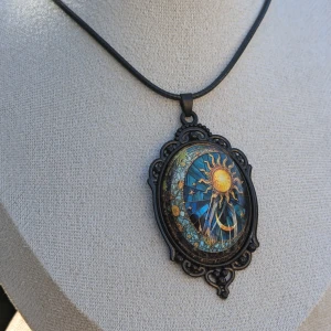 Mystiskt halsband med sol- och månmotiv - Unikt halsband med ett stort, detaljerat hänge som visar en sol och måne i en vacker blå och gul design. Hänget har en antik finish och hänger på en svart rem.NY