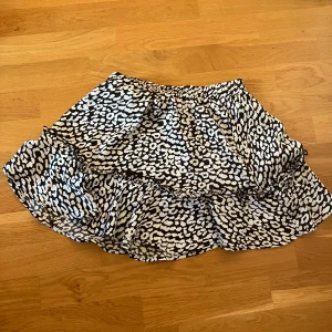 Svartvit mönstrad kjol - Säljer en superfin svartvit kortkjol med volanger. Kjolen har ett coolt mönster som påminner om leopard och är perfekt för både vardag och fest. 