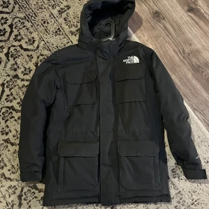 Svart parkajacka från The North Face - Säljer en snygg och varm svart parkajacka från The North Face. Jackan har en huva och flera praktiska fickor framtill. Perfekt för kalla vinterdagar!  Har pälsen till luvan liggandes