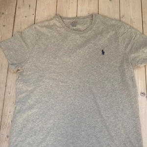 Grå t-shirt från Polo Ralph Lauren - Säljer en snygg grå t-shirt från Polo Ralph Lauren. Den har en klassisk design med korta ärmar och en broderad logga i mörkblått på bröstet. T-shirten är i bomull och har en slim passform.. Storleken är L men den sitter som en M.
