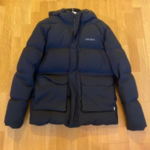 Svart pufferjacka från Les Deux - Säljer en snygg svart pufferjacka från Les Deux. Den är perfekt för vintern med sin tjocka vaddering och har en praktisk huva. ✨Helt ny skick!✨Skriv gärna om du har frågor! 