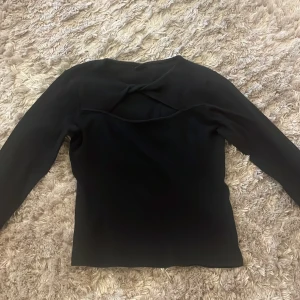 Svart långärmad topp från Gina Tricot - Säljer en stilren svart långärmad topp från Gina Tricot. Den har en unik detalj med en twistad design på ryggen som ger en öppen rygg-effekt. Perfekt för både vardag och festliga tillfällen. Toppen är i bra skick och redo för en ny ägare!