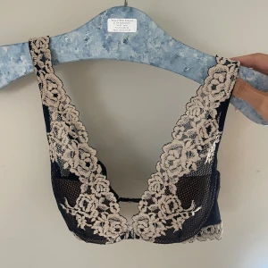 Svart spets-bh med blommönster - Snygg svart bh med vackra spetsdetaljer i beige. Den har ett blommigt mönster som ger en romantisk känsla. Perfekt för speciella tillfällen eller när du bara vill känna dig extra fin.