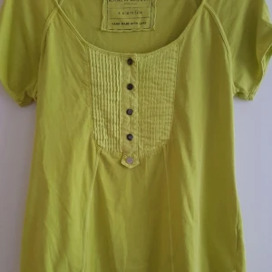 Grön topp från Karen Millen - Säljer en snygg grön topp från Karen Millen. Den har korta ärmar med en liten knappdetalj och en fin plisserad framsida med knappar. Perfekt för en avslappnad sommarlook!