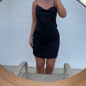 Svart axelbandslös klänning - Säljer en elegant svart klänning med smala axelband. Den är perfekt för festliga tillfällen och har en stilren design som passar alla. Klänningen är kort och har en figurnära passform som framhäver silhuetten. Aldrig använd