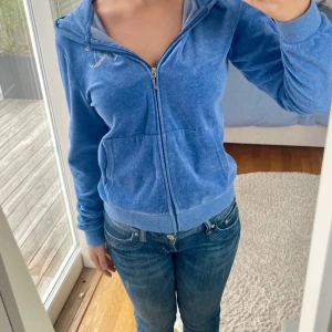 Blå huvtröja från Juicy Couture - Säljer en superskön och snygg blå luvtröja från Juicy Couture. Den har en dragkedja framtill och är dekorerad med diamanter på bröstet och ryggen. Tröjan är knappt använd och alla diamanter sitter kvar. 