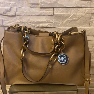 Michael kors väska  -  Brun beige Michael korsväska i medelstorlek med två stora fack samt flera små innerfack. Väskan är i skinn. Kan användas både med axelrem och med handtag. Kontakta säljaren för mer information. Nypris: 3800 kr