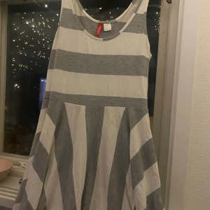 Randig klänning från H&M Divided - Säljer en superfin randig klänning från H&M Divided. Den är vit och grå med breda horisontella ränder och ärmlös design. Perfekt för sommardagar eller en avslappnad fest. Klänningen är i storlek 38 och är tillverkad i Turkiet.