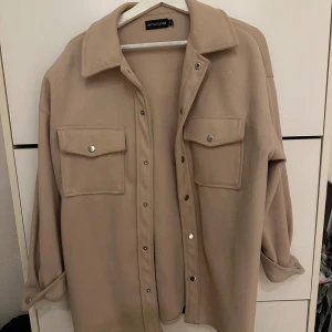 Beige overshirt från Bershka - Säljer en snygg beige overshirt från Bershka. Den har en avslappnad passform med långa ärmar och knappar framtill. Två stora fickor på bröstet ger en cool look. Perfekt för lager-på-lager under hösten eller våren! Använd 1 gång.