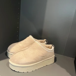 Beige mocka skor - Säljer ett par snygga och bekväma slip-ons i beige mocka. De har en tjock sula som ger extra komfort och stil. Perfekta för en avslappnad look och passar bra till både jeans och kjol. Skorna har en enkel design med dekorativ söm runt kanten.