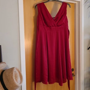 Julklänming - Väldigt fin klänning med dragkedja i sidan. Knytband bak och stretch i rygg. 100% polyester. Materialet är glansigt, svalt och lyxigt.