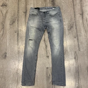 Grå jeans från Dondup - Säljer ett par snygga grå jeans från Dondup. Jeansen är väldigt unika med dessa stilrena slitningar och är där med svåra att få tag på! Det är storlek 34 och passar bra om du är runt 180-190 cm! Det är bra skick på dom, nypris runt 3500kr. 