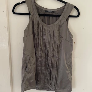 Beige ärmlös topp från Vero Moda - Säljer en snygg beige ärmlös topp från Vero Moda. Toppen har ett stilrent veckat mönster framtill och är gjord i ett mjukt och bekvämt material. Perfekt för både vardag och fest!