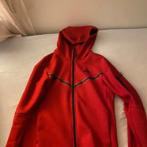 Röd fleecejacka med huva - Säljer en snygg röd nike tech fleece med huva. Perfekt nu till hösten och vintern. Säljer den pågrund av att jag inte använder den så mycket sp den bara ligger i garderoben nu. Den är knappt använd och är i riktigt bra skick.