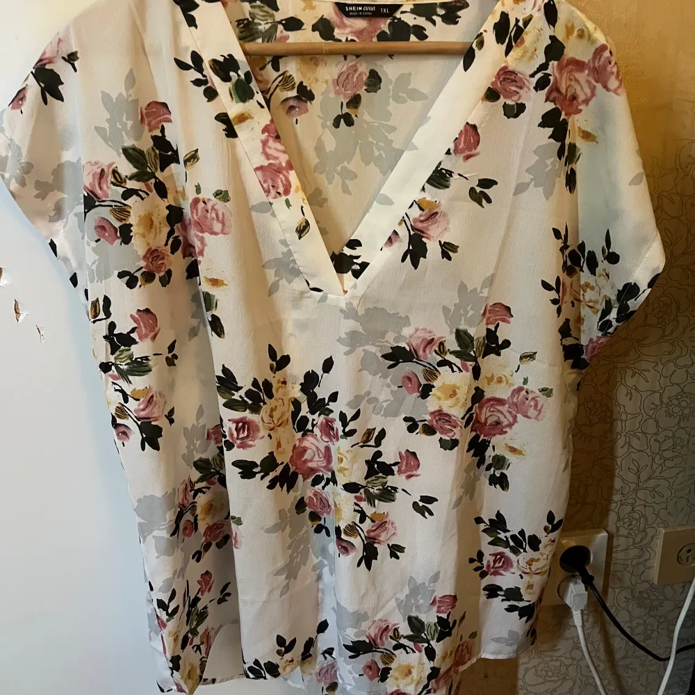 Säljer en superfin blommig blus från Shein Curve. Den är vit med ett vackert blommönster i rosa, gult och svart. Blusen har en v-ringad design och korta ärmar, perfekt för vår och sommar. Materialet är 100% polyester vilket gör den lätt och bekväm att bära.. Blusar.