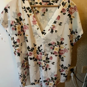 Blommig blus från Shein Curve - Säljer en superfin blommig blus från Shein Curve. Den är vit med ett vackert blommönster i rosa, gult och svart. Blusen har en v-ringad design och korta ärmar, perfekt för vår och sommar. Materialet är 100% polyester vilket gör den lätt och bekväm att bära.