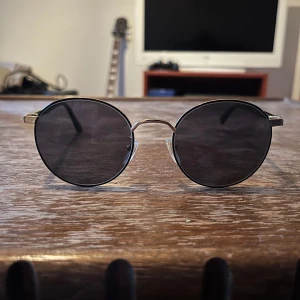 Runda solglasögon från Gucci - Säljer ett par snygga runda solglasögon från Gucci. De har en klassisk design med svarta glas och tunna guldfärgade bågar. De är i gott skick och sparsamt använda, säljer dem då de knappt kommit till användning