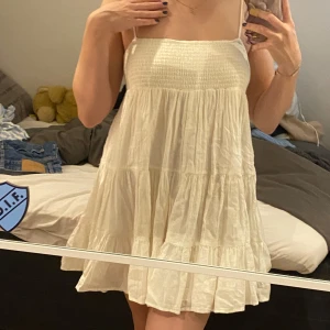 Beige sommarklänning - Säljer en superfin beige/vit sommarklänning med smala axelband och volangdetaljer. Klänningen är kort och luftig i typ linnematerial tror jag