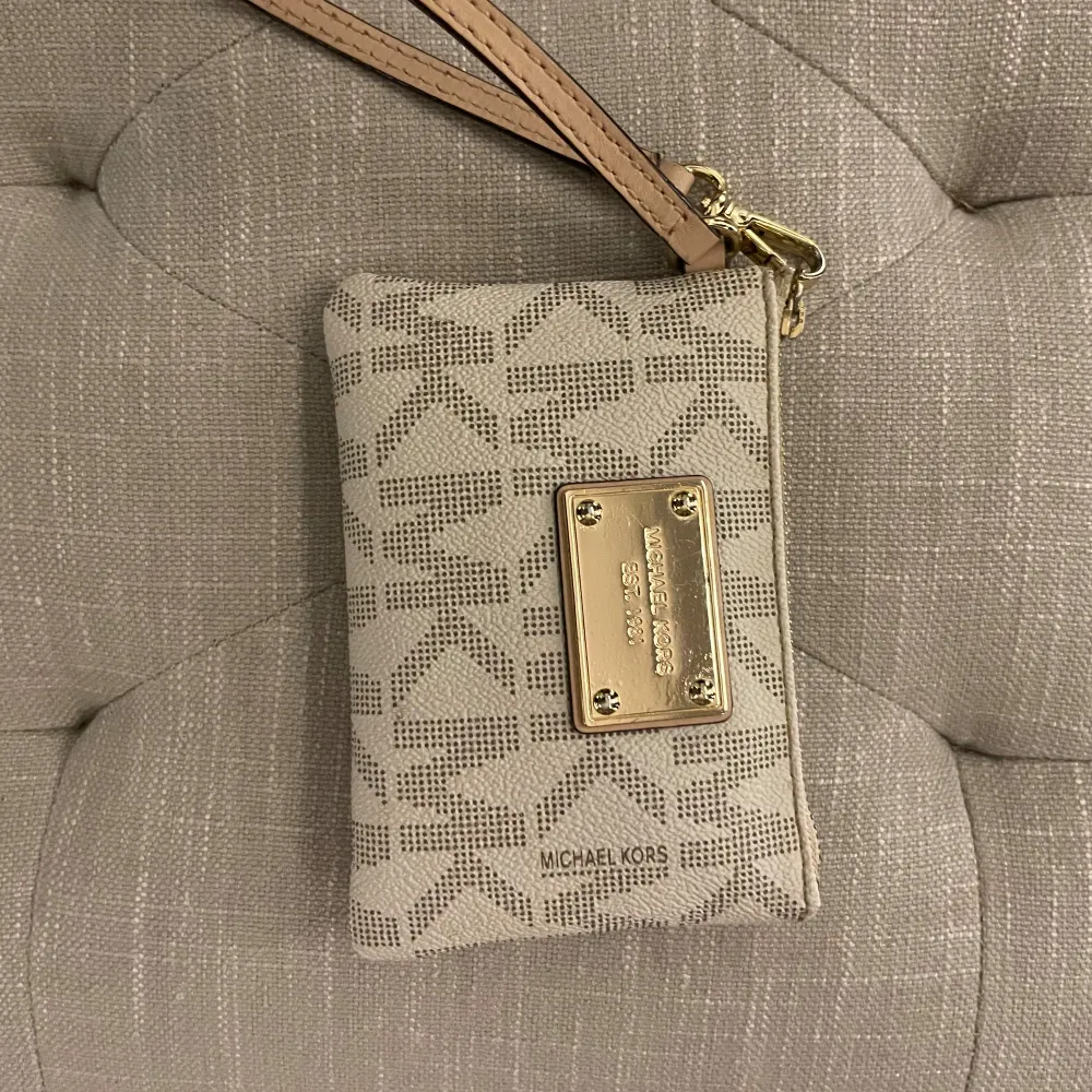 Säljer en snygg beige plånbok från Michael Kors med ett klassiskt MK-mönster. Den har en praktisk dragkedja och en stilren guldfärgad platta med logotypen på framsidan. Perfekt för att hålla ordning på kort och kontanter! Utmärkt skick . Väskor.