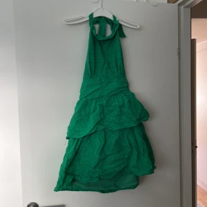 Grön klänning med spetsdetaljer - Säljer en superfin grön klänning med spetsdetaljer. Den har en halterneck-design och en dragkedja i ryggen för enkel påklädning. Perfekt för sommarens fester eller en dag på stan. Klänningen har en volangdetalj som ger den en extra touch av stil.