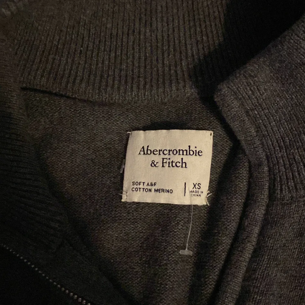 Säljer en snygg och stilren mörkgrå tröja från Abercrombie & Fitch. Den är i storlek XS och gjord av en mjuk blandning av bomull och merinoull. Perfekt för höst och vinter med sin varma och bekväma känsla. Tröjan har långa ärmar och en liten broderad logga på bröstet. Passar både till vardags och lite finare tillfällen.. Tröjor & Koftor.