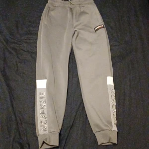 Grå mjukisbyxor från McKenzie - Säljer ett par grå mjukisbyxor från McKenzie. De har en elastisk midja och muddar vid bensluten för en bekväm passform. Byxorna har McKenzie-loggan tryckt längs benen och en liten logga på höften. Perfekta för en avslappnad dag eller träning!