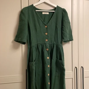 Lång klänning med fickor  - Nyskick. Mått från axlar och ner 115 cm. En ordentligt tjock och fin grön klänning med knappar längst långsidan, den har även två fickor. ECO