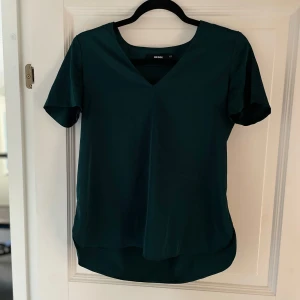Mörkgrön v-ringad topp - Säljer en snygg mörkgrön topp den har en stilren v-ringning och korta ärmar. I fint skick!💚