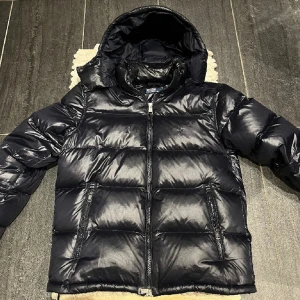 Svart pufferjacka från Polo Ralph Lauren - Säljer en snygg marinblå pufferjacka från Polo Ralph Lauren. Jackan har en glansig finish och är perfekt för kalla dagar. Den har en dragkedja framtill och en mysig huva. Perfekt för vintern!