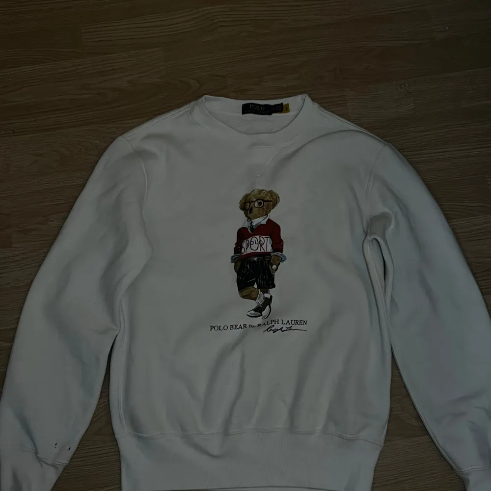 Säljer en superfin vit tröja från Ralph Lauren med den ikoniska Polo Bear på framsidan. Björnen har en röd tröja med texten 'SPORT' och ser riktigt stilig ut. Tröjan är i storlek XS och är perfekt för en casual look. Den är i bra skick och redo för nya äventyr!. Tröjor & Koftor.