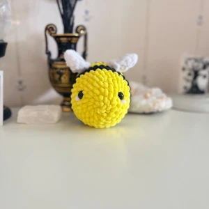 Gul och svart virkad bi-leksak - En supergullig virkad bi-leksak i gult och svart med små vita vingar. Perfekt som dekoration eller leksak. Den är mjuk och fluffig, och de små ögonen ger den ett charmigt uttryck. Passar perfekt som present eller för att liva upp rummet!