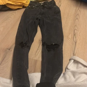 Svarta jeans med slitningar - Coola svarta jeans från 157 med slitningar på knäna. De har en klassisk femficksdesign och knappar i silverfärg. Perfekta för en avslappnad stil.