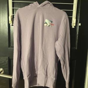 Ljuslila hoodie från Hugo - Säljer en stilren ljuslila hoodie från Hugo med en unik tryckdetalj på både fram- och baksidan. Tröjan har en klassisk passform med långa ärmar och en bekväm huva. Perfekt för en avslappnad look!