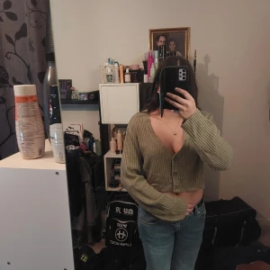 Grön ribbad kofta - Säljer en snygg grön ribbad kofta med knappar framtill. Koftan är croppad och har långa ärmar, perfekt för en avslappnad stil. Passar bra till jeans eller kjol.