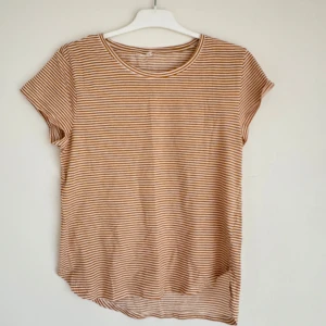 Randig t-shirt i bomull - Säljer en bekväm och stilren randig t-shirt i bomull. T-shirten har korta ärmar och ett klassiskt randigt mönster i vitt och brunt. Perfekt för en avslappnad look.