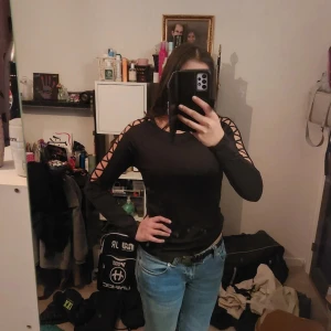 Svart långärmad träningströja med snörning - Snygg svart långärmad topp med snörningsdetaljer längs ärmarna. Perfekt för en cool och trendig look. Passar bra till jeans eller kjol.