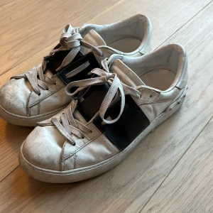 Valentino sneakers i vitt och svart - Snygga Valentino sneakers i vitt med svarta detaljer. Skorna har klassisk snörning och en stilren design. Perfekta för en trendig look.