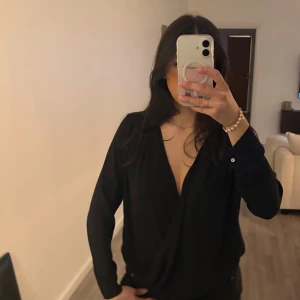 Svart blus med v-ringning - Snygg svart blus med djup v-ringning och långa ärmar. Perfekt för både fest och vardags. 