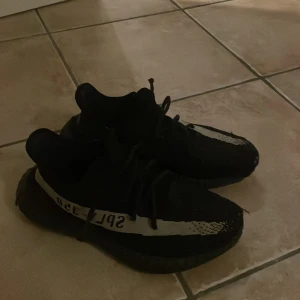 Yeezy sneakers - Snygga svarta Adidas Yeezy sneakers med en distinkt vit rand och texten 'SPLY-350' på sidan. Skorna har en modern design med snörning och en bekväm sula. ÄKTA